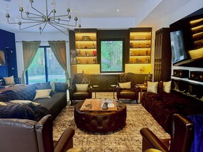 Una sala moderna con muebles de cuero, un televisor grande y una estantería con botellas.