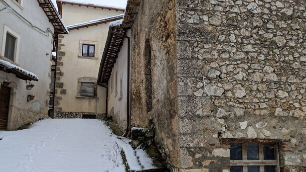 Un estrecho callejón cubierto de nieve entre edificios de piedra, con una puerta de madera y ventanas.