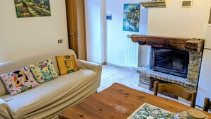 Sala de estar con un sofá, almohadones coloridos, una mesa de centro de madera, chimenea y vista a una puerta y pasillo.