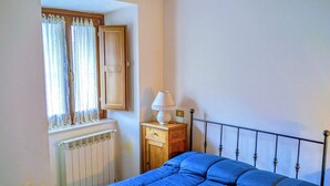 Un dormitorio con cama, un radiador, una ventana con cortinas, una lámpara y una luz en el techo.