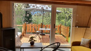 A cozy room with a sliding glass door leading to an outdoor deck with a wooden fence, a table with chairs, and a potted bonsai tree.