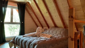 A bedroom with a sloped ceiling, a bed with a grey duvet, and a window with curtains.