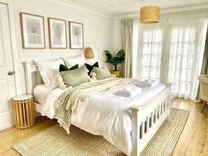 Une chambre à coucher bien rangée, avec un lit, des tables de chevet, un luminaire suspendu et une fenêtre avec des rideaux.
