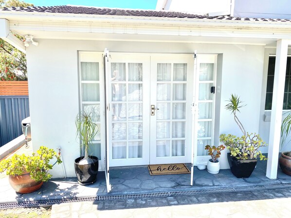 A white house with a glass door, potted plants, and a 'hello' mat.