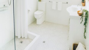Ein modernes Badezimmer mit Duschkabine aus Glas, Toilette, Waschbecken mit Spiegel und einem Fenster mit hängenden Pflanzen.