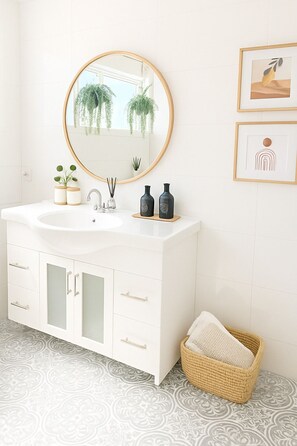 A bathroom with a white vanity, a round mirror, two framed artworks, and a woven basket.