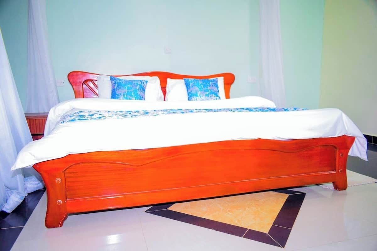 Ein Bett mit Holzbettgestell und weißer Bettwäsche, einer gemusterten Tagesdecke und blauen Kissen.