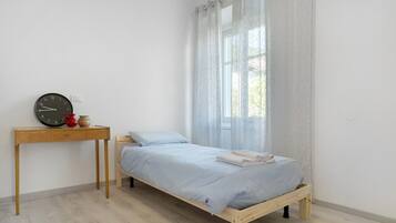 Ein Schlafzimmer mit einem Bett, einem Holztisch, einer Uhr und einem Fenster mit Vorhängen.