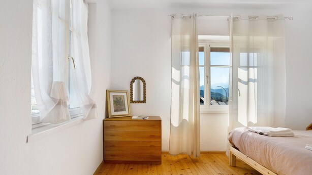 Ein Schlafzimmer mit einem Holzbett, einem Schminktisch, einem Spiegel und einem Fenster mit transparenten Vorhängen.