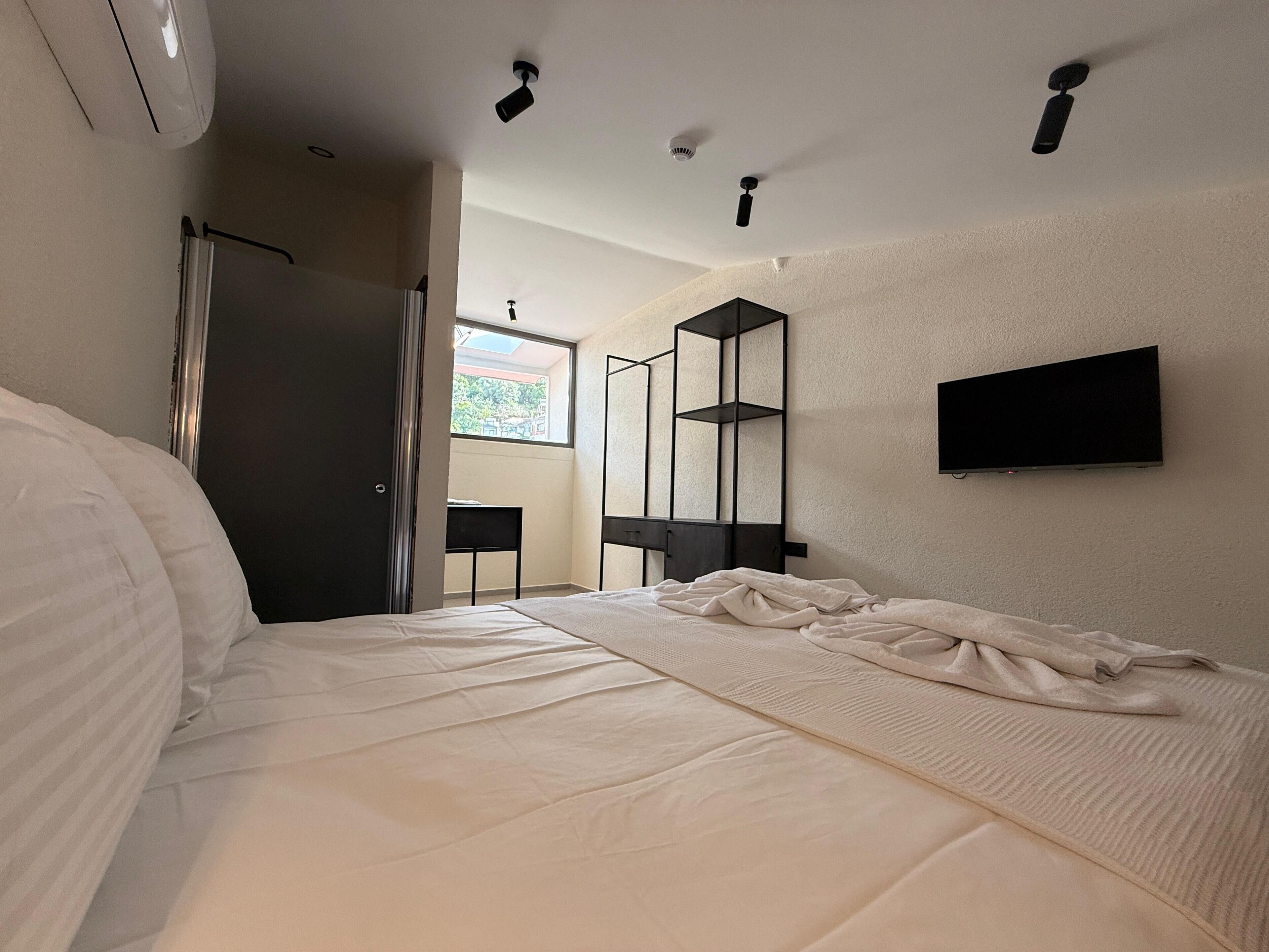 A modern bedroom with a large bed, a TV mounted on the wall, and a window providing a view of the outdoors.