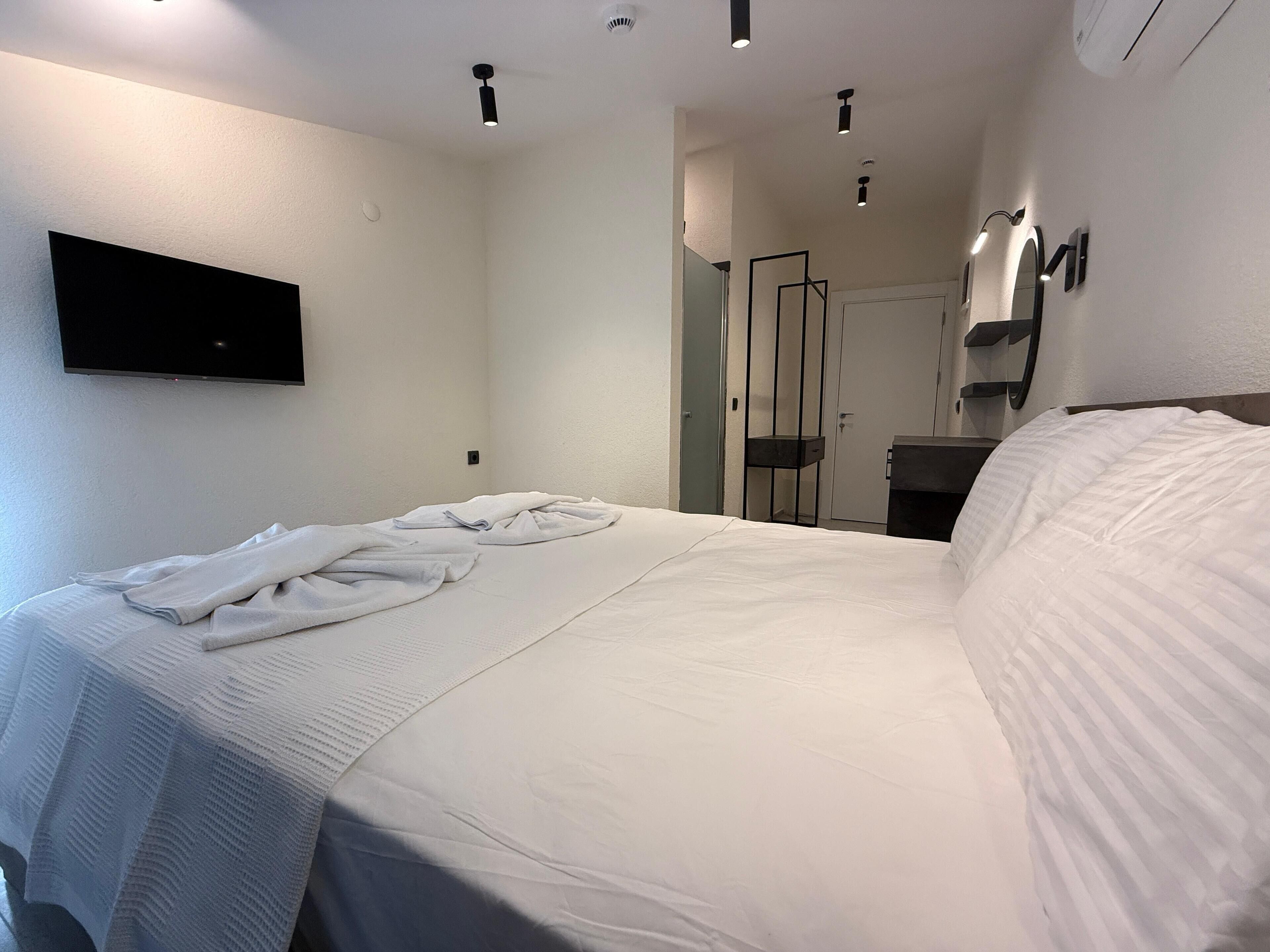 A hotel room with a bed, a TV mounted on the wall, a mirror, and a door.