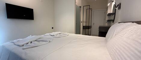 A hotel room with a bed, a TV mounted on the wall, a mirror, and a door.