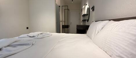 A hotel room with a neatly made bed, a bedside table, a mirror, and a wall-mounted air conditioning unit.