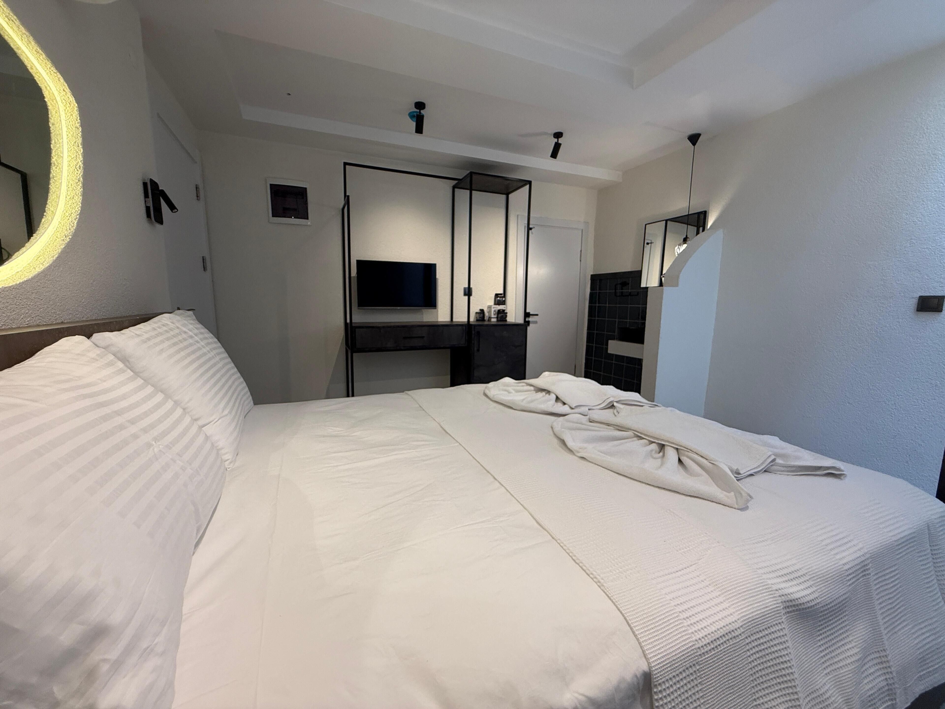 A modern hotel room with a large bed, a television, and a bathroom with a mirror.