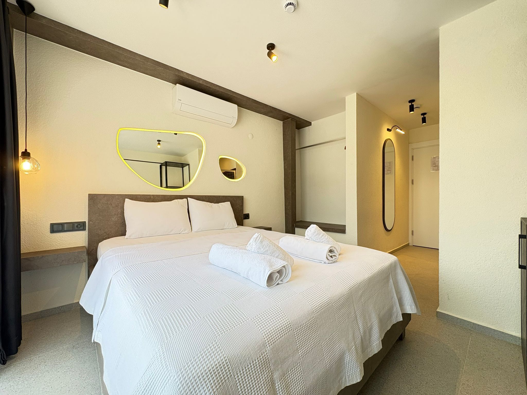 Una habitación de hotel con una cama grande, un espejo y un aire acondicionado de pared.