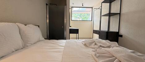 Un dormitorio con cama, escritorio y ventana con vistas a zonas verdes.
