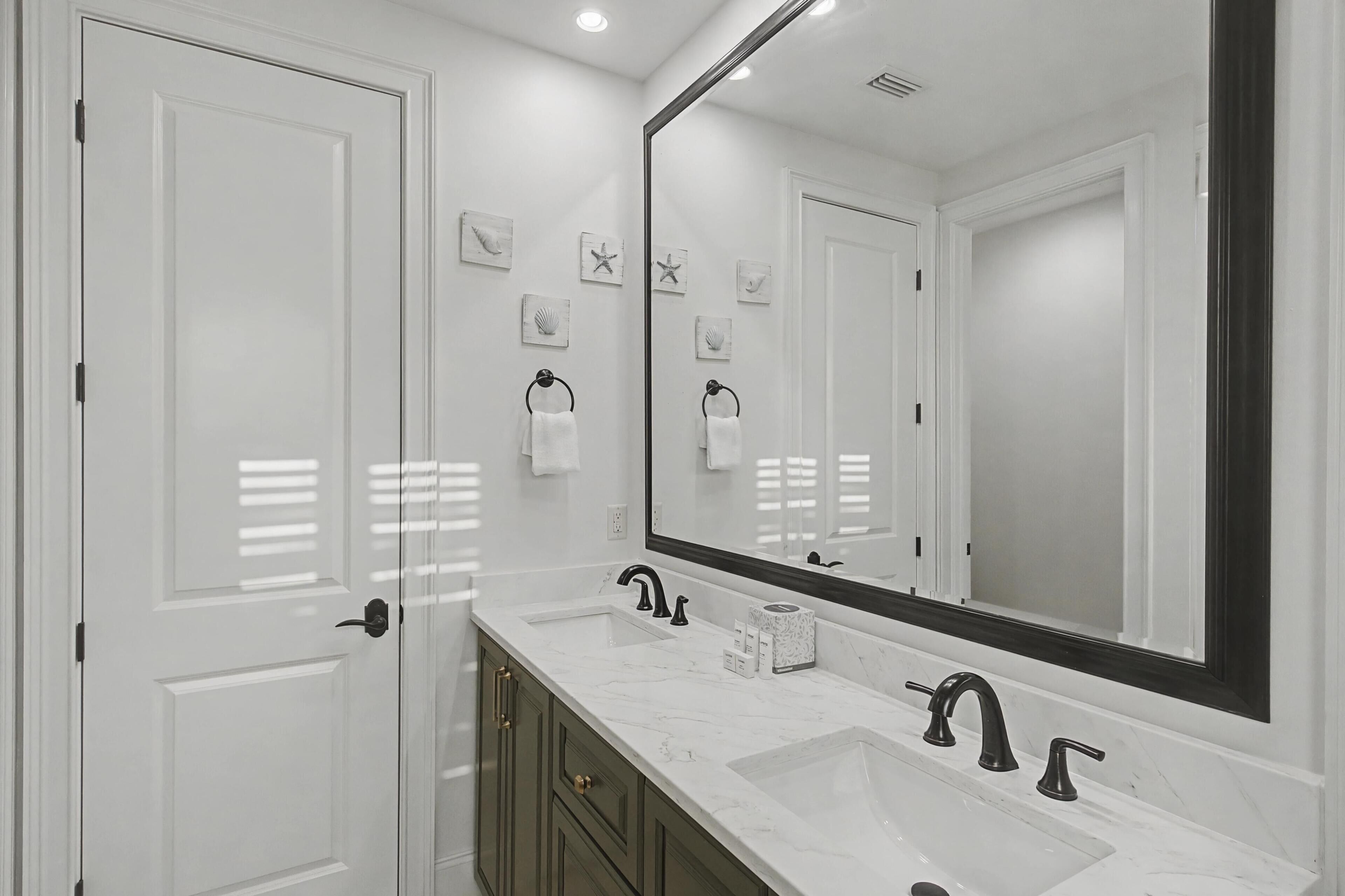 A modern bathroom with two sinks, a large mirror, and a door with a towel rack.