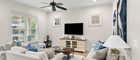 A living room with a ceiling fan, a flat-screen TV, a coffee table, and a sofa set.