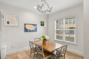 Ein Esszimmer mit Holztisch, Stühlen, einer Chandelier, einer Karte und einem Fenster mit Jalousien.