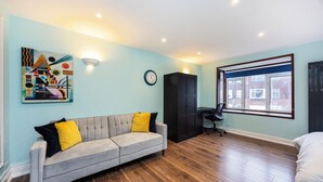 Een kamer met een grijze bank, een zwarte kast, een bureau met een stoel, en een groot raam.