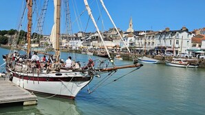 Ein historisches Segelschiff liegt im Hafen, im Hintergrund eine Stadt.