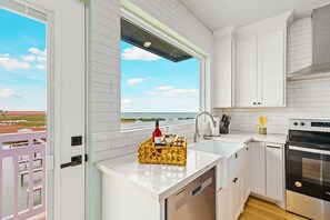 A modern kitchen with white cabinetry, a stainless steel oven, and a window overlooking a scenic view. - Skip the letdown in South Padre! 🌊 Pelican 301 is a designer boho-chic condo with stunning bay views. Experience hotel-grade luxury with the comfort of a curated home. 24/7 concierge and a coastal reset await. Welcome to the Born Again life. ✨ (SOUTH PADRE ISLAND)