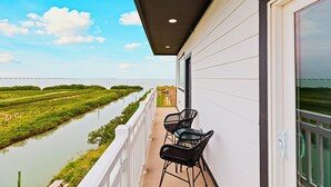 Un balcón con dos sillas y una mesa con vistas a un río y vegetación.
