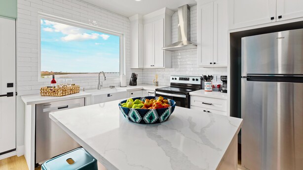 Una cocina moderna con armarios blancos, un refrigerador de acero inoxidable y un amplio ventanal con vistas.