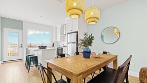 Una cocina moderna con armarios blancos, una mesa de comedor de madera y dos lámparas colgantes amarillas.