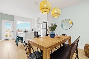 A modern kitchen with white cabinets, a wooden dining table, and two hanging yellow pendant lights. - Skip the letdown in South Padre! 🌊 Pelican 301 is a designer boho-chic condo with stunning bay views. Experience hotel-grade luxury with the comfort of a curated home. 24/7 concierge and a coastal reset await. Welcome to the Born Again life. ✨ (SOUTH PADRE ISLAND)