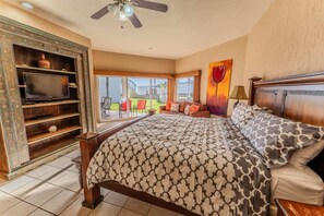 A bedroom with a bed, a TV on a wooden shelf, a ceiling fan, and a view of the outdoors. - Villa 10, Beachfront Las Palmas Resort (Puerto Peñasco)