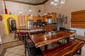 A kitchen with wooden cabinets, a granite countertop, a stainless steel refrigerator, and a dining area with a wooden table and benches. - Villa 10, Beachfront Las Palmas Resort (Puerto Peñasco)