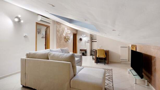 A modern living room with a sofa, a TV on a stand, and a dining area with a chair and table.