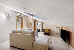 Ein modernes Wohnzimmer mit einer Couch, einem Fernseher auf einem Schrank und einem Essbereich mit Stuhl und Tisch.