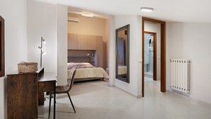A bedroom with a bed, a desk with a chair, a mirror, and a radiator.