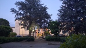A parking lot with trees, a building with a gated entrance, and a fence.
