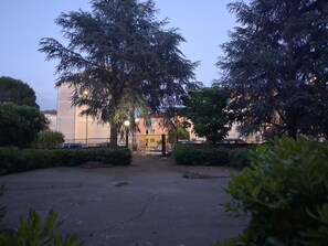 Ein Parkplatz mit Bäumen, ein Gebäude mit befestigtem Eingang und einem Zaun.