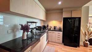 Een moderne keuken met lichte houtkasten, een zwart aanrecht, een roestvrijstalen spoelbak en een zwarte koelkast, plus een vaas met gedroogde bloemen.