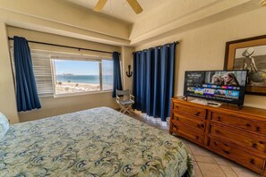 Quarto com uma cama, cômoda, televisão e vista para a praia.