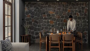 Un salon moderne avec un mur en pierre, un coin repas avec une table dressée pour quatre personnes et un canapé agrémenté d’un coussin à motifs.