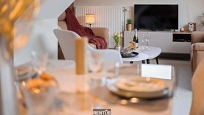 Ein modernes Wohnzimmer mit einer Couch, einem Couchtisch und einem Fernseher. Auf dem Tisch steht eine Lampe, eine Pflanze und eine Flasche.