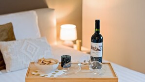 Ein ordentlich gemachtes Bett mit einem Holztablett, auf dem eine Weinflasche, Gläser und Snacks stehen, was eine entspannte Atmosphäre vermittelt.