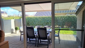 Ein Patio mit Tisch und Stühlen, einem Blumentopf und Blick auf einen Hecken- und ein Ziegeldach.