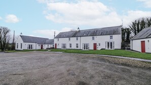 A row of white buildings with red doors, a gravel driveway, and a grassy area. - Foyle Cottage (Strabane)