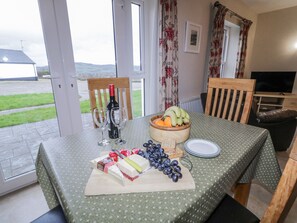 Een eettafel gedekt met een fles wijn, glazen, een fruitschaal, kaas en druiven.