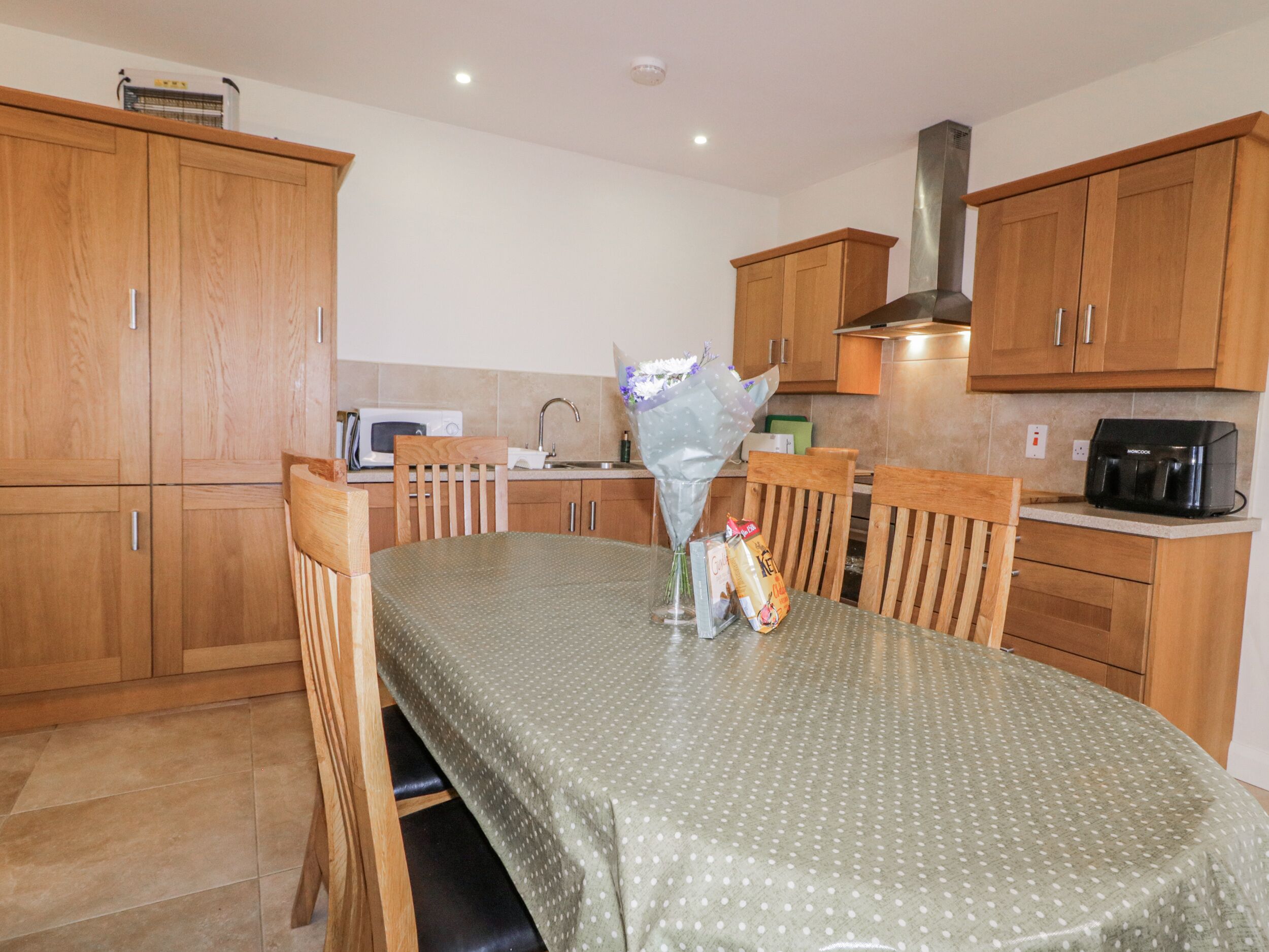 A kitchen with wooden cabinets, a dining table with a green polka dot tablecloth, and a bouquet of flowers.