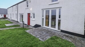A white two-story house with a red door, a small garden, and a paved walkway. - Foyle Cottage (Strabane)
