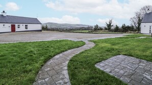 A rural property with a paved driveway leading to a white building with a red door, surrounded by grassy areas and stone walls. - Foyle Cottage (Strabane)