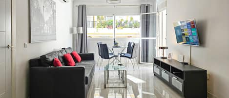 A modern living room with a black sofa, red cushions, a glass coffee table, and a TV on a stand.