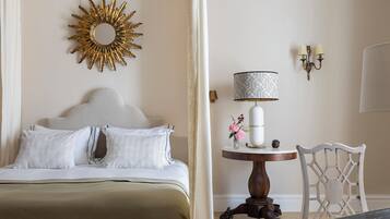 A bedroom with a bed, a round table with a lamp, a chair, and a decorative wall piece.